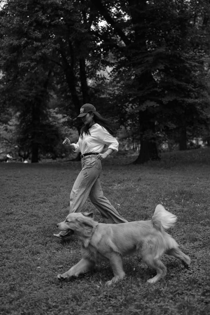 Black and white photograph of a woman walking her dog through a park